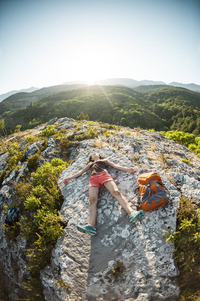 Tyttö, jolla on reppu, makaa vuoren huipulla auringonlaskun aikaan. Nainen harrastaa joogaa. Meditaatio on kaukana sivilisaatiosta. Kauniin luonnon mietiskelyä. Näkymä vuorille
. - Valokuva, kuva