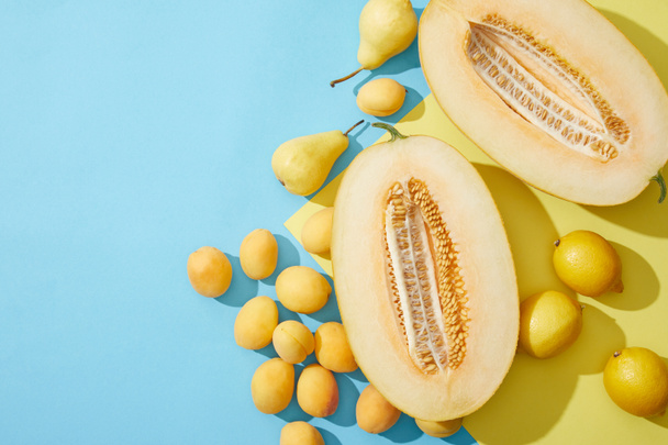 bovenaanzicht van citroenen, zoete rijpe meloen, peren en abrikozen op blauwe en gele achtergrond - Foto, afbeelding