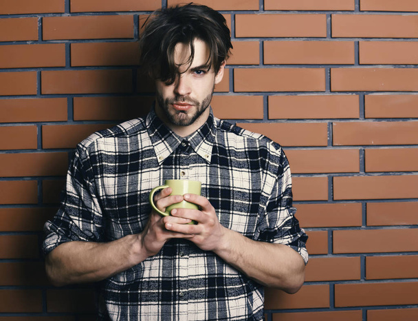 serious face holding yellow cup on textured brick wall background, copy space. handsome guy holding cup on brick wall background - Foto, immagini