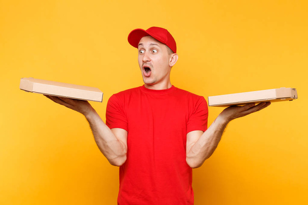 Delivery man in rode dop, t-shirt geven voedsel volgorde pizzadozen geïsoleerd op gele achtergrond. Mannelijke werknemer pizzaman of koerier in uniform Italiaanse pizza in kartonnen flatbox houden. Dienstverleningsconcept - Foto, afbeelding