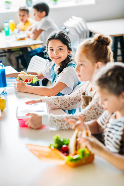 weinig gelukkig schoolmeisjes nemen lunch op Schoolcafetaria - Foto, afbeelding