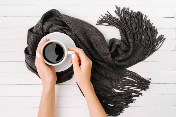 female hands holding cup of coffee wrapped in black scarf  - Фото, зображення