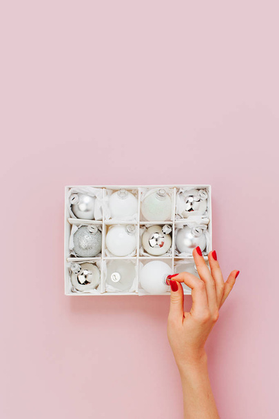 Female hand putting bauble in box with christmas baubles collection on pink background - 写真・画像