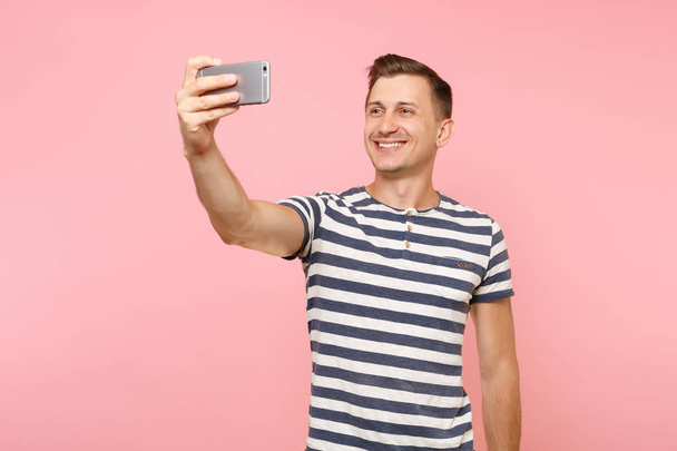 T-shirt giyen gülümseyen genç adam portresi çizgili selfie modern cep telefonu üzerinde gidişli pastel pembe arka plan izole atış yapıyor. İnsanlar samimi duygular yaşam tarzı kavramı. Reklam alanı - Fotoğraf, Görsel