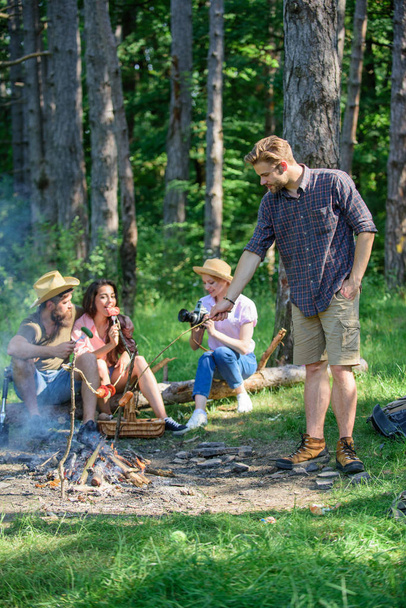 Tourists sharing thoughts about hike sit on log. Picnic with friends in forest near bonfire. Company having hike picnic nature background. Hikers sharing impression of walk forest. Summer tradition - 写真・画像