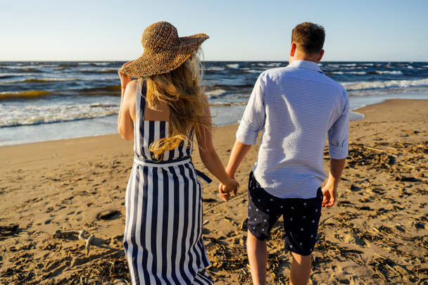 πίσω όψη του στοργικό ζευγάρι κρατώντας τα χέρια και το περπάτημα σε αμμώδης παραλία θερινή ημέρα - Φωτογραφία, εικόνα