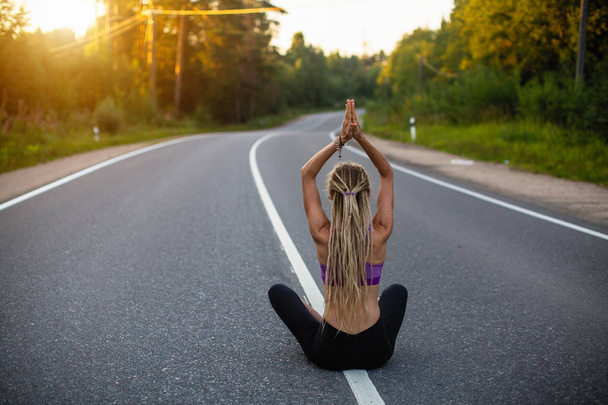 Yoga féminin assis au milieu d'une route autoroutière méditant en position Lotus
. - Photo, image