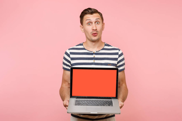 Portrait de jeune homme tenant à la main un ordinateur portable avec écran vide noir vierge espace de copie isolé sur fond rose pastel. Les gens sincères émotions concept de style de vie. Espace publicitaire
 - Photo, image