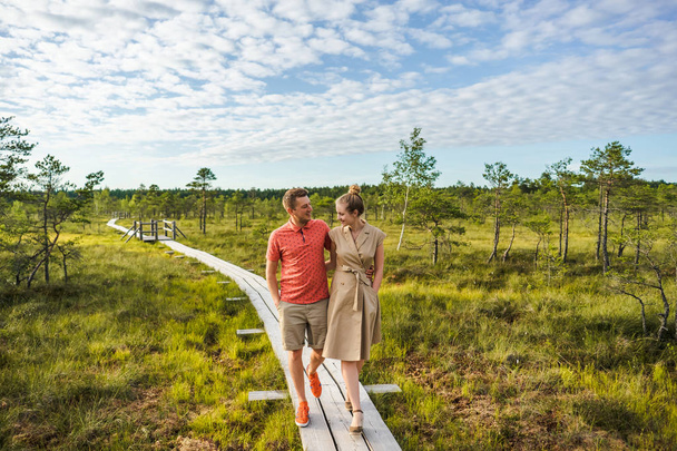 couple souriant amoureux marchant sur un pont en bois avec des plantes vertes et ciel bleu sur le fond
 - Photo, image