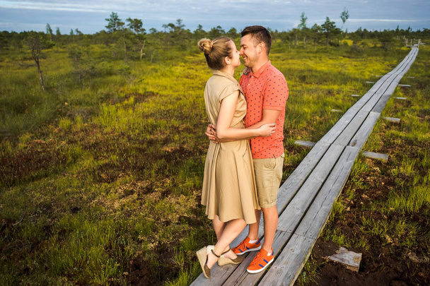 lachende paar in hou van knuffelen elkaar op houten brug met groene planten op achtergrond - Foto, afbeelding