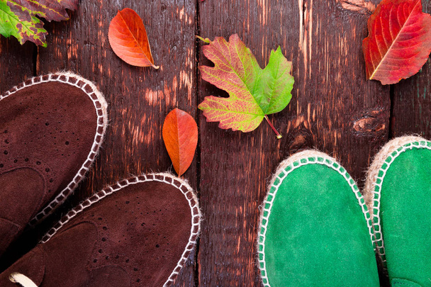 茶色と緑色の男スエード ブーツ サンダル葉を持つ木製の背景。秋や冬の靴。2 つのペア。フラットを置く. - 写真・画像