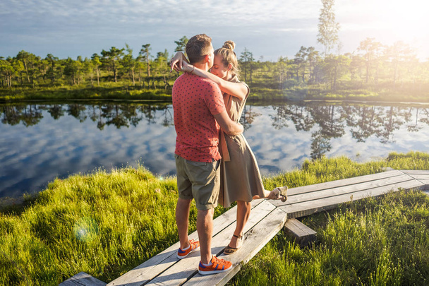 Verliebtes Paar umarmt sich auf Holzbrücke mit grünen Bäumen und Fluss im Hintergrund - Foto, Bild