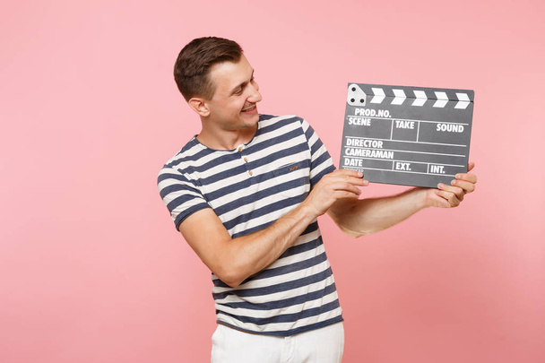Portrait de jeune homme portant un t-shirt rayé tenant un film noir classique faisant clin d'oeil isolé sur fond rose pastel tendance. Les gens sincères émotions concept de style de vie. Espace publicitaire
 - Photo, image