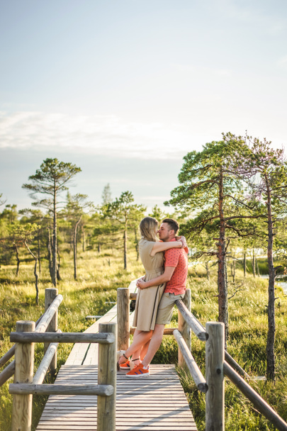 Μερική άποψη του στοργικό ζευγάρι αγκαλιάζει την ξύλινη γέφυρα με πράσινα φυτά και σε φόντο μπλε του ουρανού - Φωτογραφία, εικόνα
