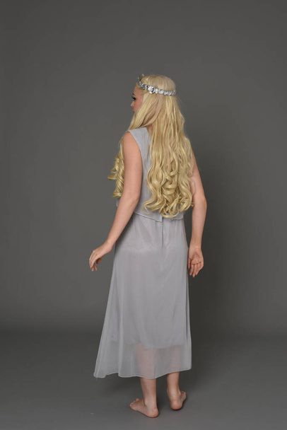 Ganzkörperporträt eines blonden Mädchens mit Kleid und Krone. stehend mit dem Rücken zur Kamera posieren. grauer Studiohintergrund. - Foto, Bild