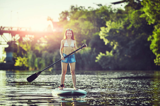 Attractive young woman stand up paddle surfing - Valokuva, kuva