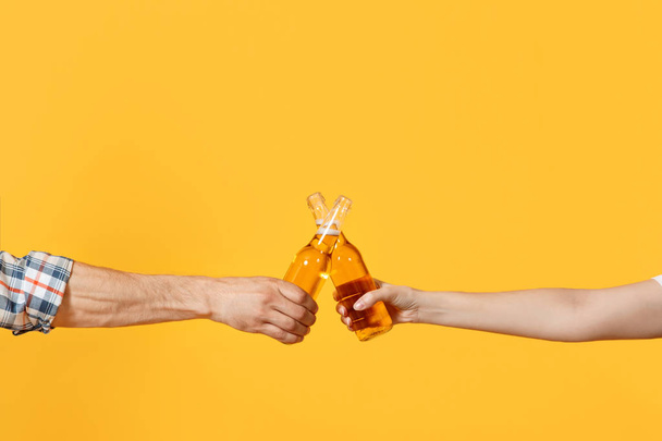 Close up cropped of woman and man two hands horizontal holding lager beer glass bottles and clinking isolated on yellow background. Sport fans cheer up. Friends leisure lifestyle concept. Copy space - Fotografie, Obrázek