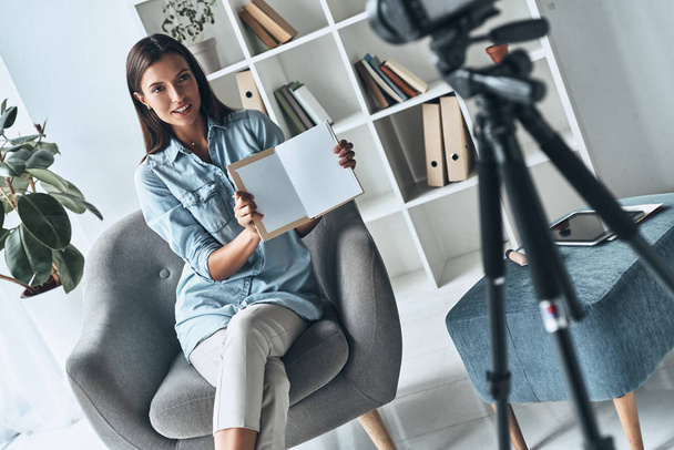 brunette woman showing paper blank for copy space and smiling while making new video indoors - Photo, image