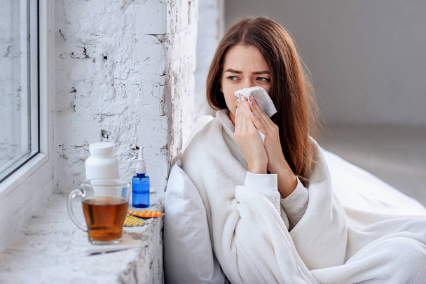 Cold and flu. Sick woman caught cold, feeling illness and sneezing in paper wipe. Closeup of beautiful unhealthy girl covered in blanket wiping nose. Healthcare concept. - Photo, image
