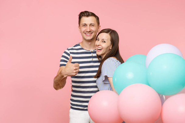 Portrait of young happy smiling couple in love. Woman and man in blue clothes celebrating birthday holiday party on pastel pink background with colorful air balloons. People sincere emotions concept - Photo, Image