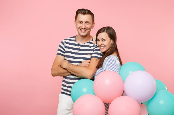 Portrait of young happy smiling couple in love. Woman and man in blue clothes celebrating birthday holiday party on pastel pink background with colorful air balloons. People sincere emotions concept - Фото, изображение