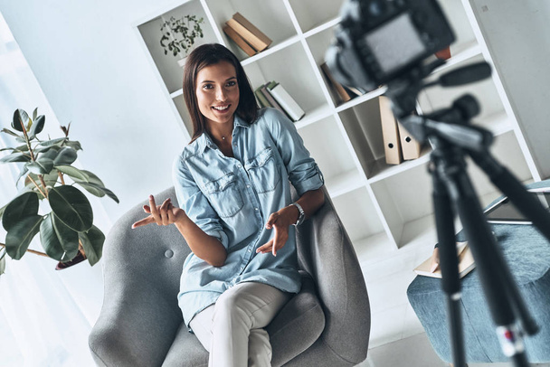 Giving good advice. Attractive young woman gesturing and smiling while making new video indoors - Foto, Imagen