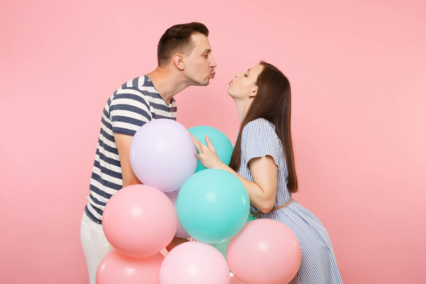 幸せなキス カップル愛の肖像画。女性と誕生日の祝日を祝う青い服の男は、カラフルな気球とパステル ピンクの背景に党します。人々 の心から感情の概念 - 写真・画像