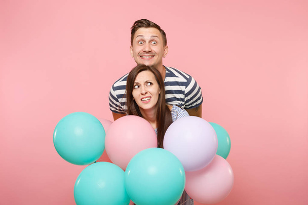 Портрет молодой веселой сумасшедшей влюбленной пары. Женщина и мужчина в голубой одежде празднуют день рождения на розовом фоне с красочными воздушными шарами. Понятие искренних эмоций
 - Фото, изображение