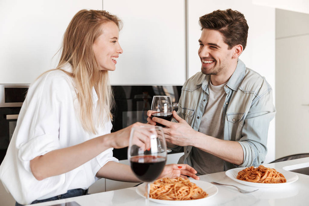 Image of young happy loving couple in kitchen have a dinner drinking wine eating spaghetti. - Foto, immagini