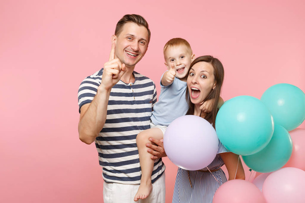 Portrét mladé šťastní rodiče držet v náručí, líbání pÛdû dítě dítě syn chlapeček, slaví narozeniny dovolená stranou na pastelově růžové pozadí s barevné s vrtulovým pohonem. Koncept upřímné emoce - Fotografie, Obrázek