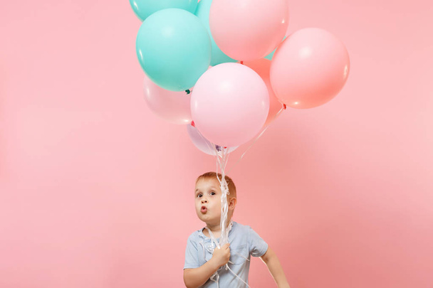 Playful little cute child baby boy holding bunch of colorful air balloons, celebrating birthday holiday party on pastel color pink background. Family day kids children childhood lifestyle concept - Photo, Image