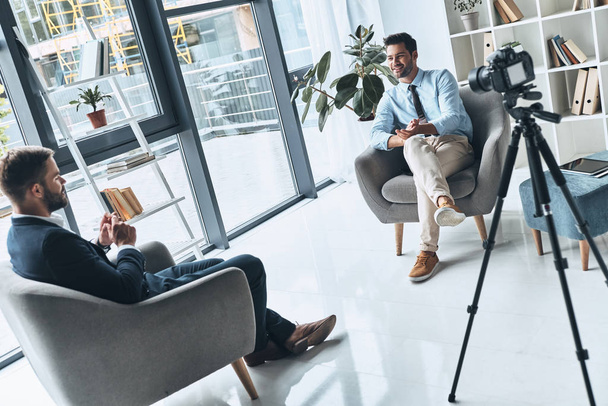 man met interview sessie met journalist in moderne studio met opname camera op statief     - Foto, afbeelding