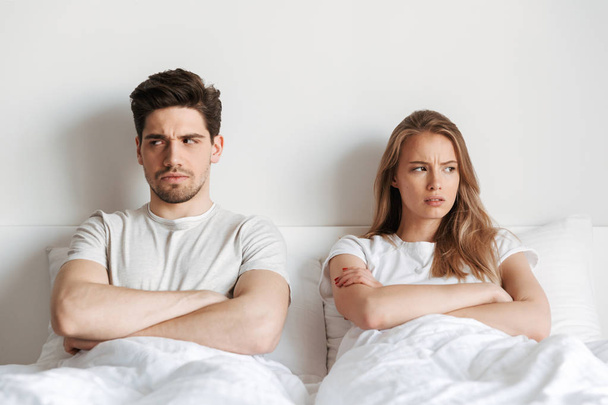 Image of young displeased negative offended loving couple lies in bed quarrel. - Photo, image