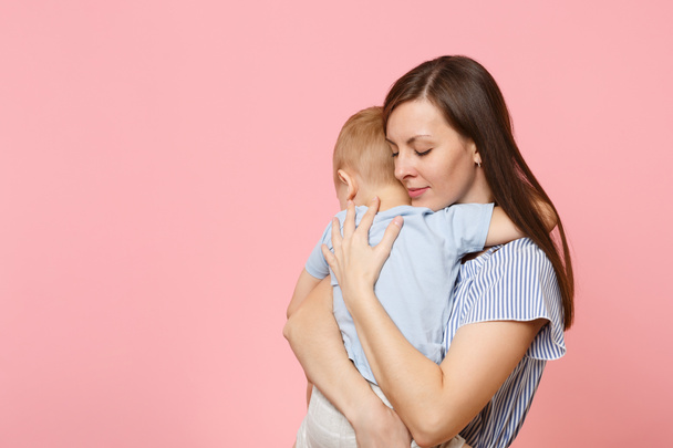 Portrait happy young family. Mother keep in arms, tender embrace, gently hugs child kid son baby boy on pastel pink background. Sincere emotions, fondness, Mother's Day, parenthood, childhood concept - Photo, Image