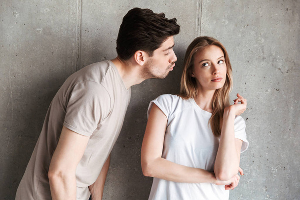 Portrait of outraged displeased woman expressing unwillingness while handsome man kissing her cheek isolated over gray background - Foto, afbeelding