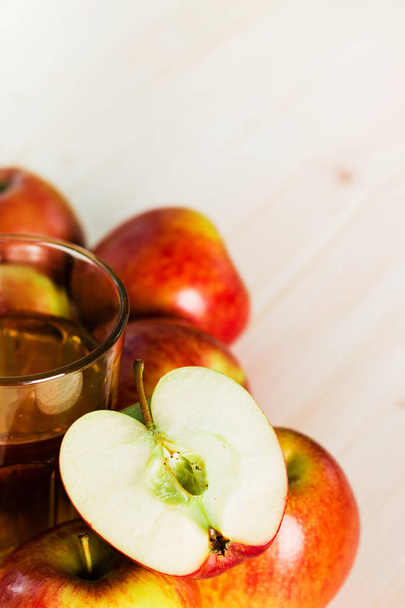Glass of fresh apple cider and half apple near autumn apples. Wooden background, space for text. Autumnal background. - Photo, Image