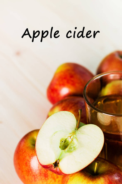 Glass of fresh apple cider and half apple near autumn apples. Wooden background, text apple cider. Autumnal background. - Foto, imagen