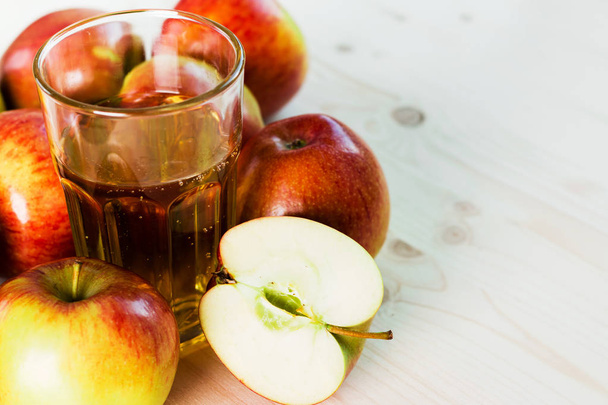 Glass of fresh apple cider and half apple near autumn apples. Wooden background, space for text. Autumnal background. - Photo, Image