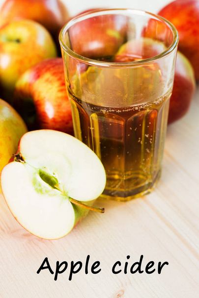 Glass of fresh apple cider and half apple near autumn apples. Wooden background, text apple cider. - Фото, изображение
