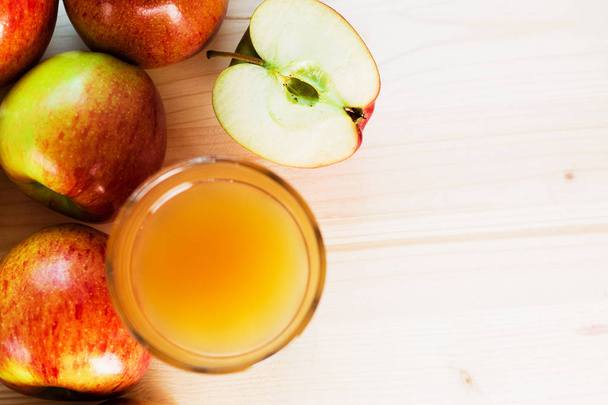 Ein Glas frischer Apfelsaft und ein halber Apfel neben herbstlichen Äpfeln. Holzhintergrund, Blick von oben, Platz für Text. - Foto, Bild