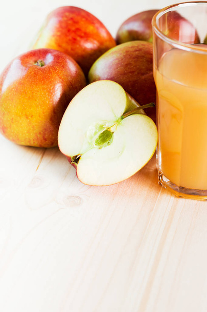 Ein Glas frischer Apfelsaft und ein halber Apfel neben herbstlichen Äpfeln. Holzhintergrund, Raum für Text. Herbstlicher Hintergrund. - Foto, Bild