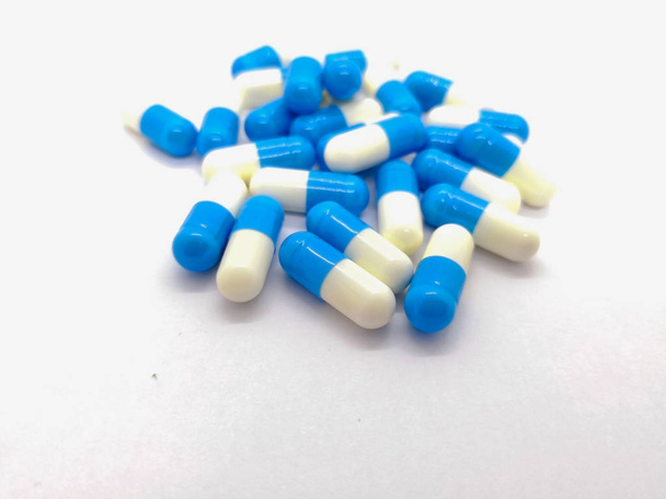 Medicatie en gezondheidszorg concept. Veel blauw-witte capsules van Dicloxacilline 250 mg. geïsoleerd op een witte achtergrond, gebruikt voor de behandeling van veel verschillende soorten infecties veroorzaakt door bacteriën. Selectieve focus en kopieer ruimte. - Foto, afbeelding