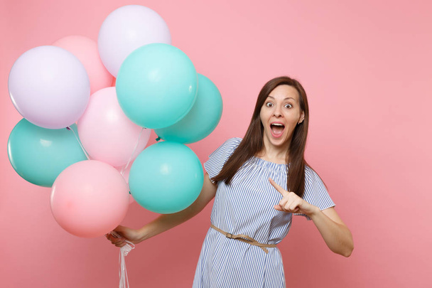 Retrato de mulher alegre surpresa com boca aberta em vestido azul apontando dedo indicador em balões de ar coloridos isolados em fundo rosa. Festa de aniversário de férias, as pessoas conceito emoções sinceras
 - Foto, Imagem