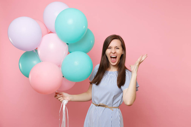 Porträt einer verrückten jungen glücklichen Frau in blauem Kleid, die schreiend bunte Luftballons hält und die Hände isoliert auf leuchtend rosa Hintergrund ausbreitet. Geburtstagsparty, Menschen aufrichtige Emotionen Konzept - Foto, Bild