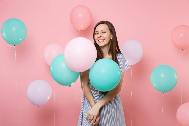 Portrait of beautiful smiling young happy woman wearing blue striped dress holding colorful air balloons on bright trending pink background. Birthday holiday party, people sincere emotions concept - Foto, Imagen