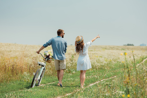 back view of couple with retro bicycle in summer field with wild flowers - Photo, Image