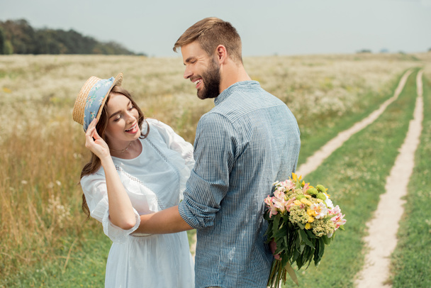 sonriente hombre ocultar ramo de flores silvestres para novia detrás de vuelta en el campo de verano
 - Foto, imagen