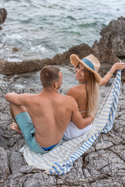 высокий угол обзора красивой счастливой молодой пары, сидящей вместе на скалистом пляже в Черногории
 - Фото, изображение