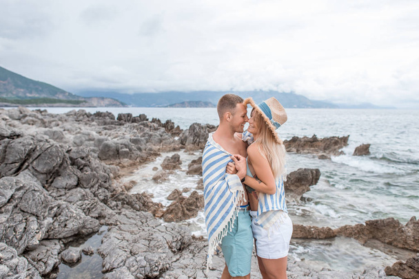 side view of beautiful happy young couple in love hugging and smiling each other on rocky beach in montenegro - Foto, Imagen