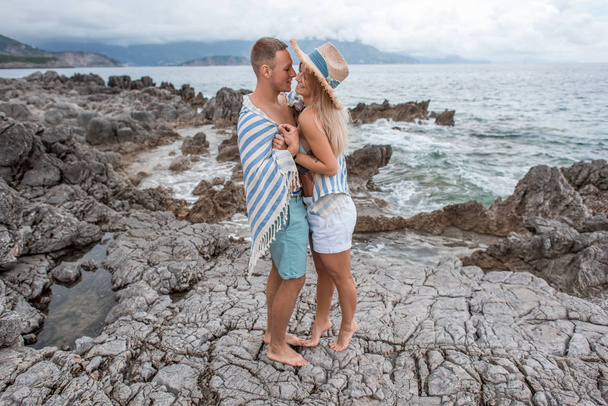 Seitenansicht eines schönen jungen Paares, das zusammen steht und sich am felsigen Strand in Montenegro umarmt - Foto, Bild